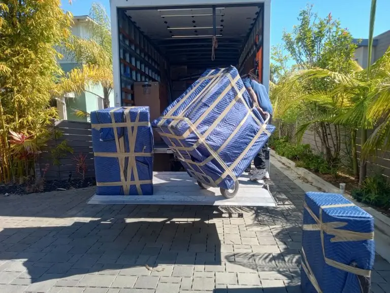 Mover rolling padded furniture onto the lift-gate of a One Stop truck